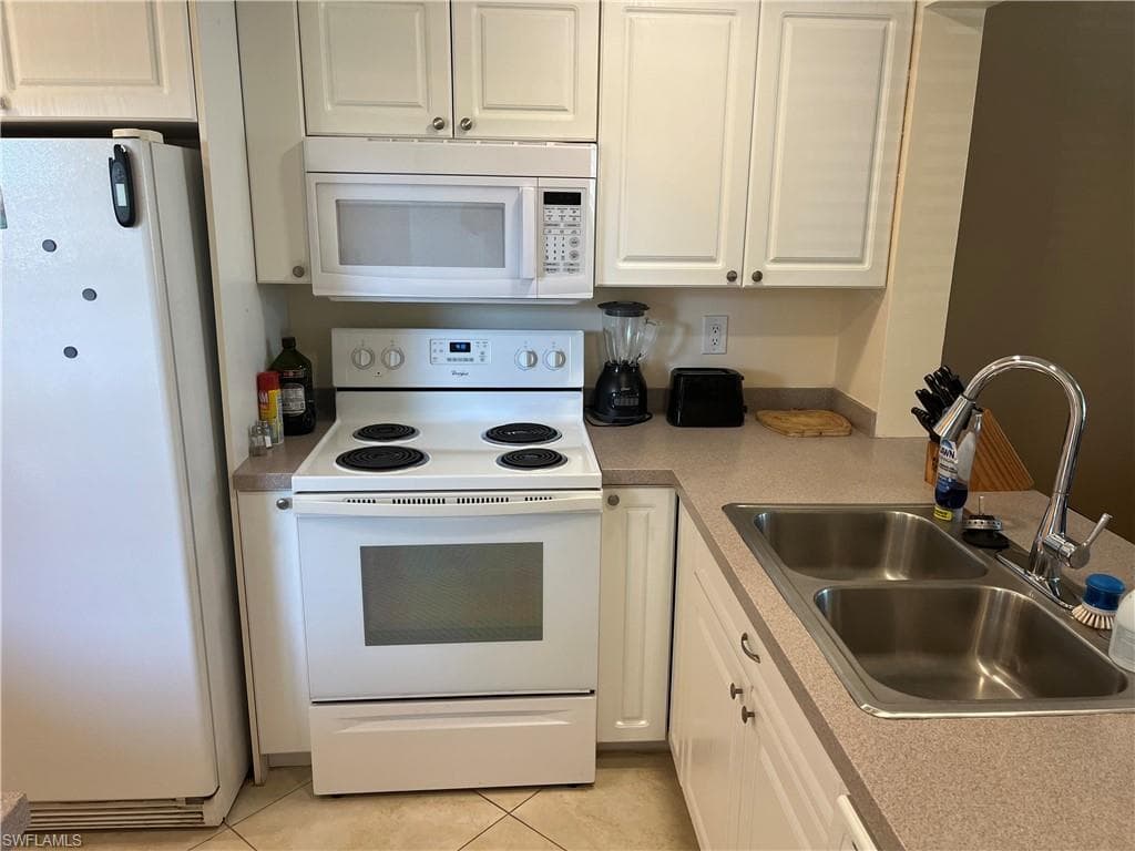 Kitchen featuring white appliances, white cabinets, light tile patterned floors, and light countertops