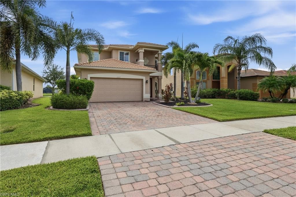 Two-story stucco exterior featuring a tile roof, an integrated garage, a paver driveway, and mature palm trees