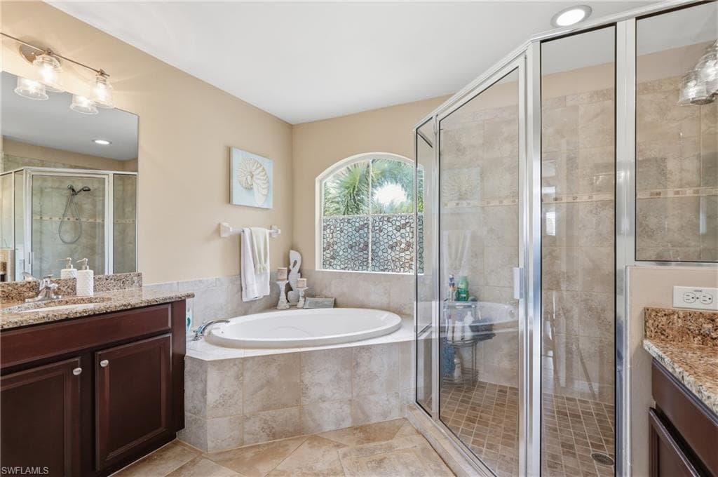 Bathroom featuring a spacious soaking tub, an arched window, and a separate glass-enclosed shower