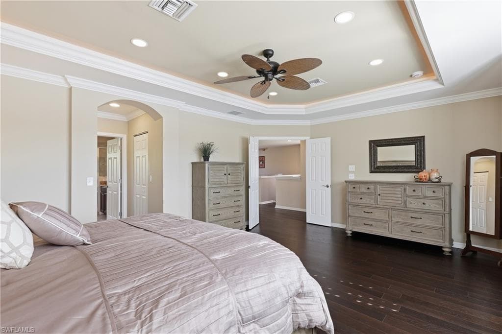 Spacious room featuring dark wood-finish flooring, a tray ceiling with recessed lighting and crown molding, and an arched entryway