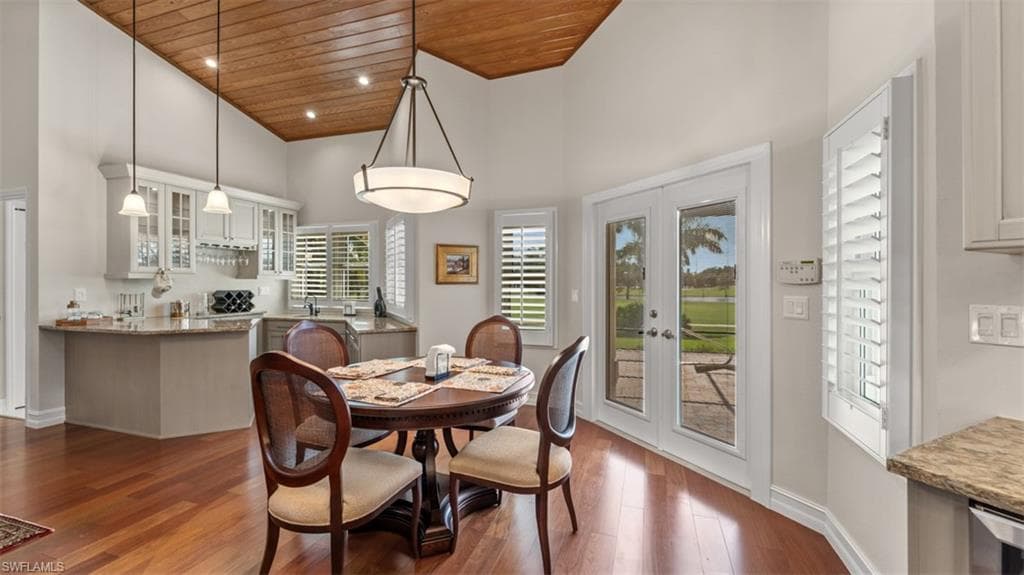 Open-concept dining space with wood-finish flooring, a vaulted wood-plank ceiling, and a built-in wet bar featuring upper glass-front cabinetry and pendant lighting