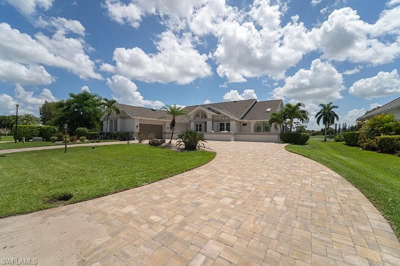 Expansive paver driveway leading to a residence featuring arched windows, a two-car garage, and a light-toned exterior