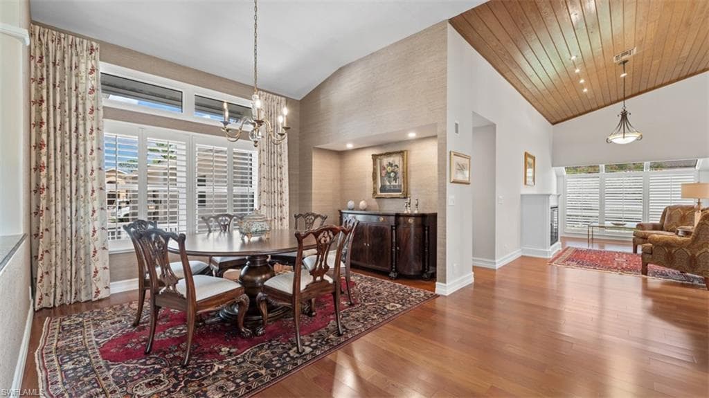 Dining area featuring vaulted ceilings with wood-finish paneling, hardwood flooring, and a chandelier