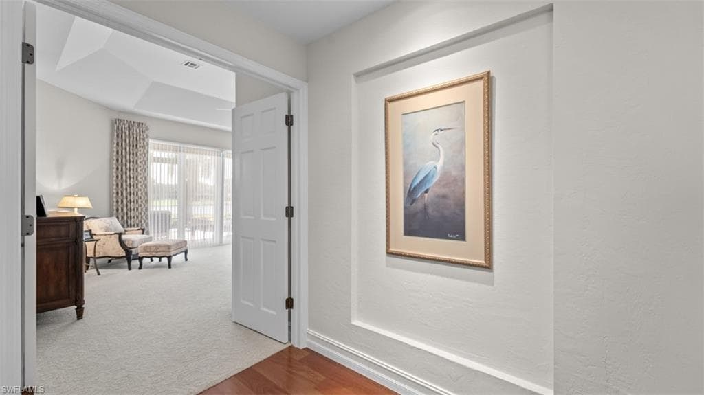 Wood-finish flooring in the entryway leads to a carpeted room featuring a tray ceiling, large sliding glass doors, and patterned drapery