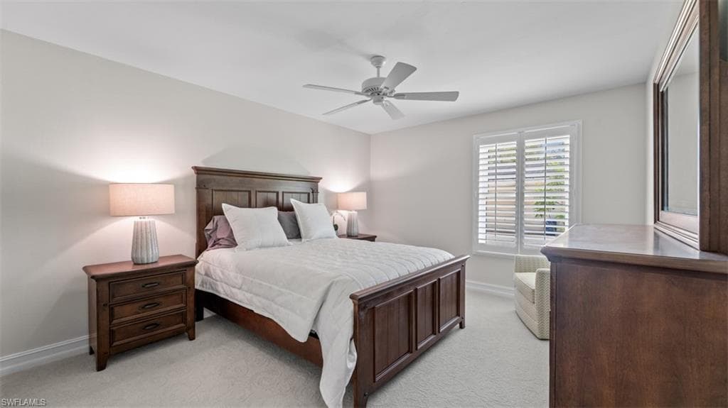 Spacious bedroom with light-colored carpeting, a ceiling fan, and a large window featuring white plantation shutters