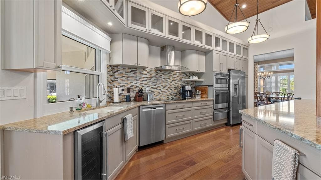 Kitchen featuring wood-finish flooring, light-toned cabinetry, stainless steel appliances, a mosaic tile backsplash, and granite countertops