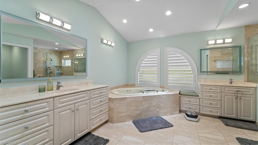 Vaulted ceiling bathroom featuring dual vanities with integrated sinks and light-toned cabinetry