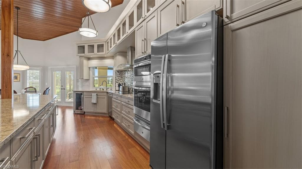 Gourmet kitchen featuring stainless steel appliances, extensive cabinetry with glass-front uppers, granite countertops, wood-finish flooring, and a vaulted wood-paneled ceiling