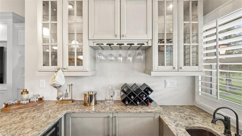 Kitchenette, Serving Bar, featuring light-toned cabinetry with glass-front uppers, a built-in wine glass rack, and a stone countertop