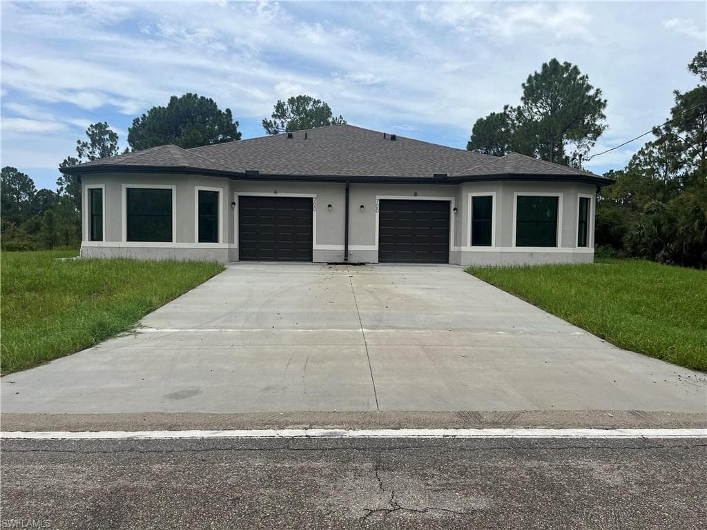 Contemporary duplex featuring a light gray exterior, dark garage doors, and a dark shingle roof