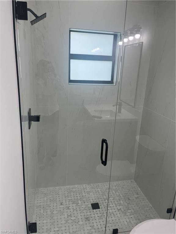 Glass-enclosed shower featuring a rainfall showerhead and mosaic tile flooring