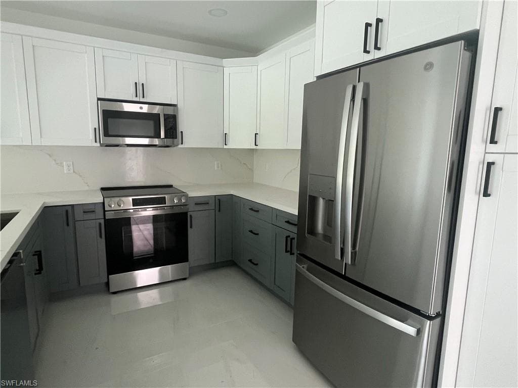 Modern kitchen featuring white shaker-style cabinetry with stainless steel hardware, two-tone cabinetry design with contrasting gray lower cabinets, quartz countertops, stainless steel appliances including a French-door refrigerator, electric range, and over-the-range microwave, and a neutral tile backsplash