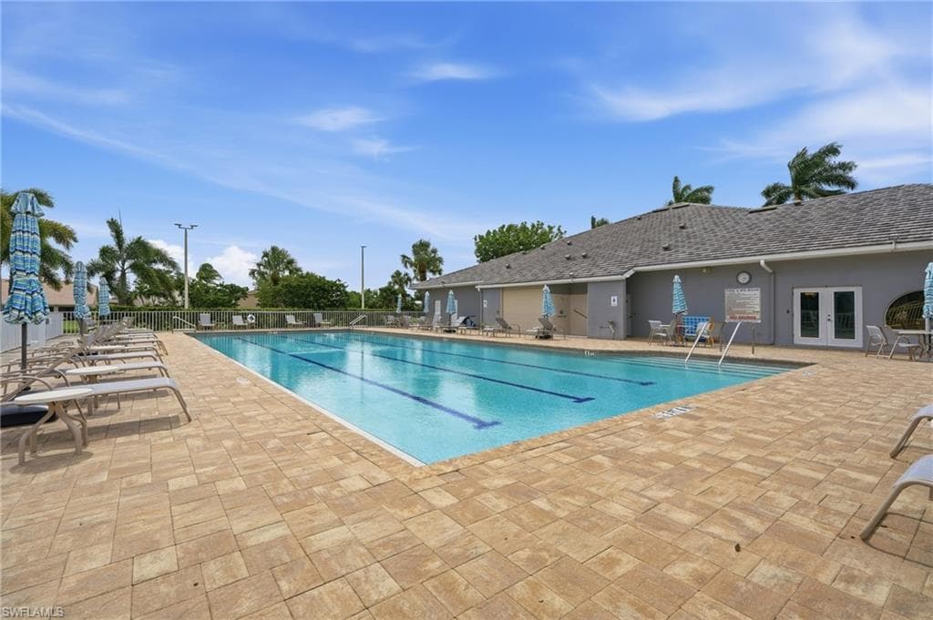 Community swimming pool featuring a lap lane, surrounding paver patio, and adjacent clubhouse building with double doors