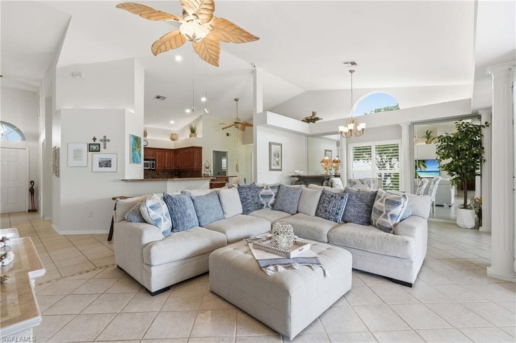 Vaulted ceilings featuring a palm-leaf style ceiling fan, tile flooring throughout, and a half-wall kitchen bar with a granite countertop