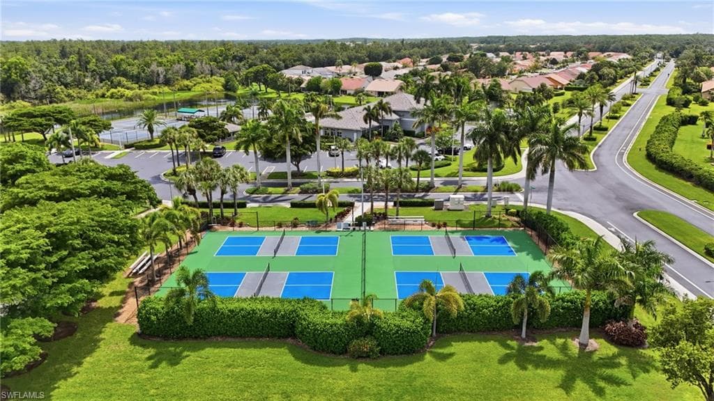 Four pickleball courts with green and blue surfaces, surrounded by mature landscaping and palm trees