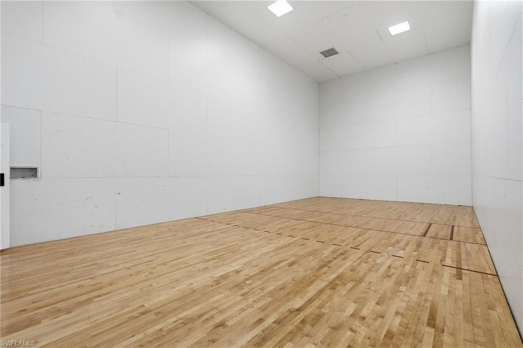 Dedicated indoor court featuring light wood-finish flooring with court markings, white paneled walls, and recessed ceiling lighting