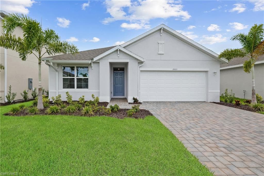 Contemporary single-story residence featuring a light gray exterior, an integrated garage, a paver driveway, a blue paneled front door, and established landscaping with palm trees