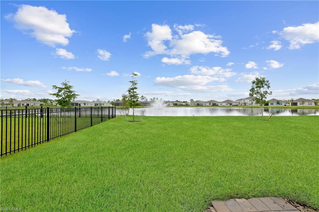 Expansive green lawn with a black metal fence, overlooking a water feature with a fountain