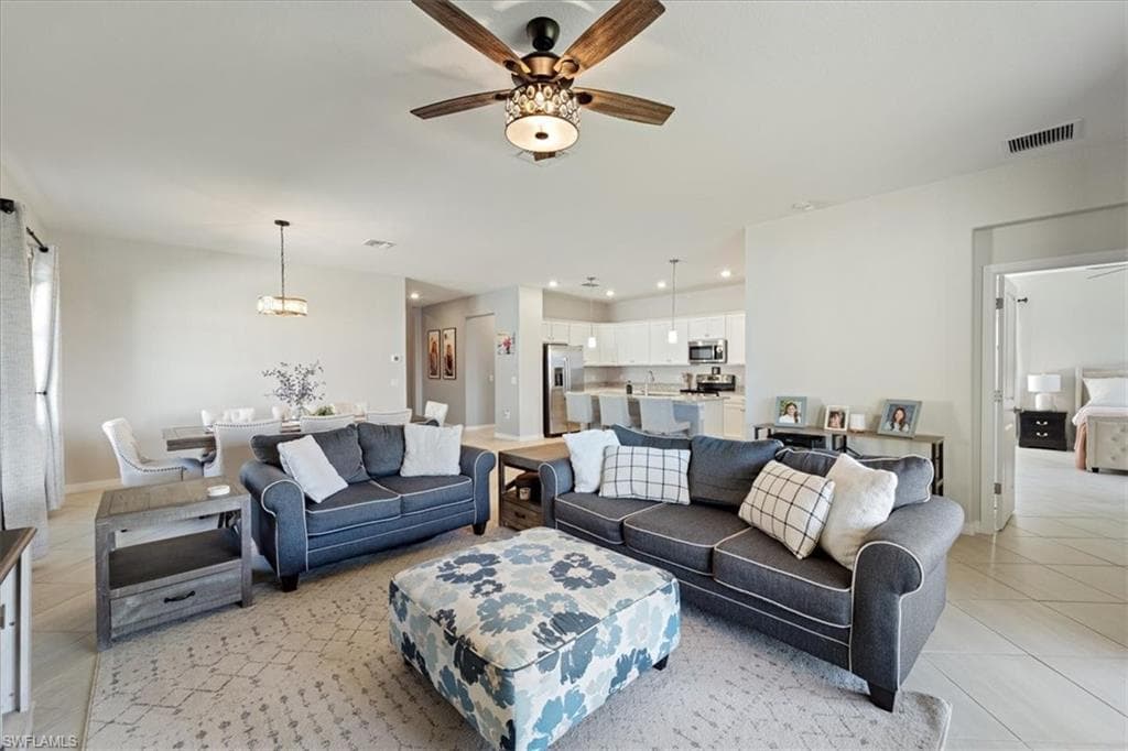 Open-concept living area featuring light-toned walls, tile flooring, and a ceiling fan with integrated lighting