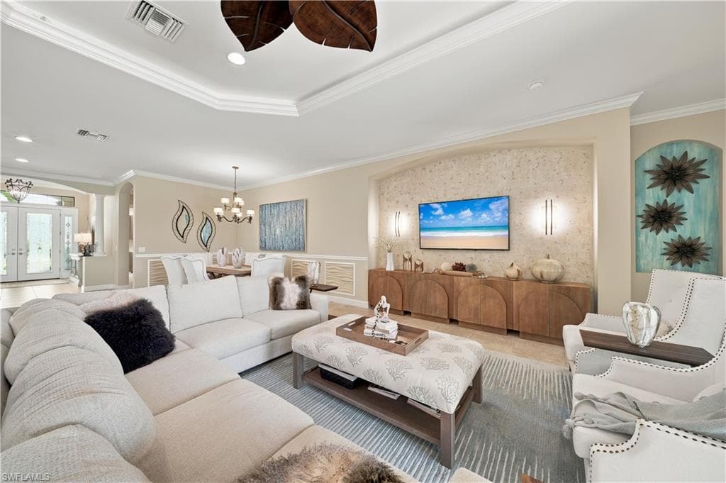 Open-concept living area featuring tray ceilings with crown molding, recessed lighting, and a textured accent wall
