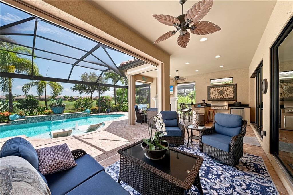 Expansive screened lanai featuring a swimming pool with water features, paver decking, and a built-in outdoor kitchen with grill and refrigerator