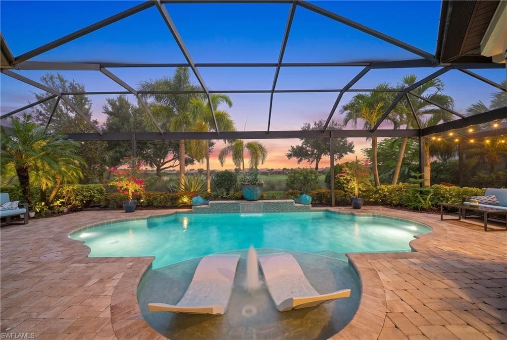 Screened-in swimming pool featuring a curved design, integrated sun shelf with chaise lounges, and an elevated spa with a waterfall feature