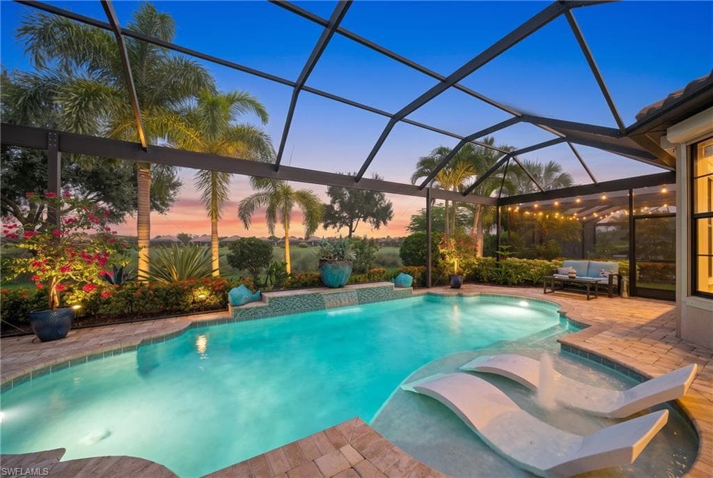Screened lanai featuring a free-form pool, integrated spa, sun shelf, brick paver decking, and lush landscaping