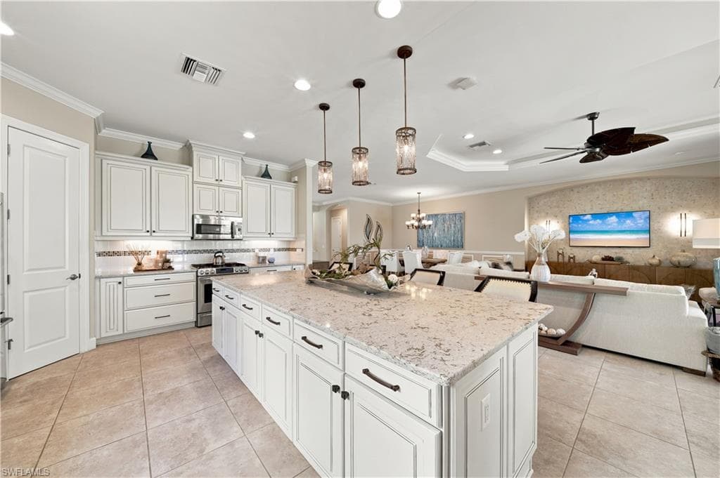 Open-concept kitchen featuring an expansive island with a light-toned countertop, white cabinetry with dark hardware, stainless steel appliances, and tile flooring