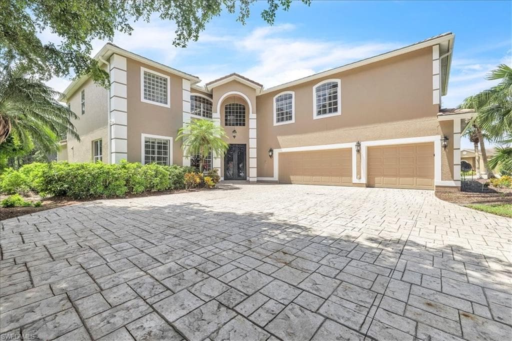 Stucco exterior featuring decorative white banding, an arched entryway, and a stamped concrete driveway