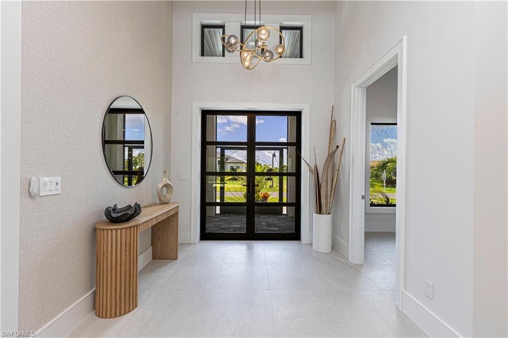 Two-story foyer featuring a contemporary chandelier, transom windows, and double entry doors with segmented glass panels