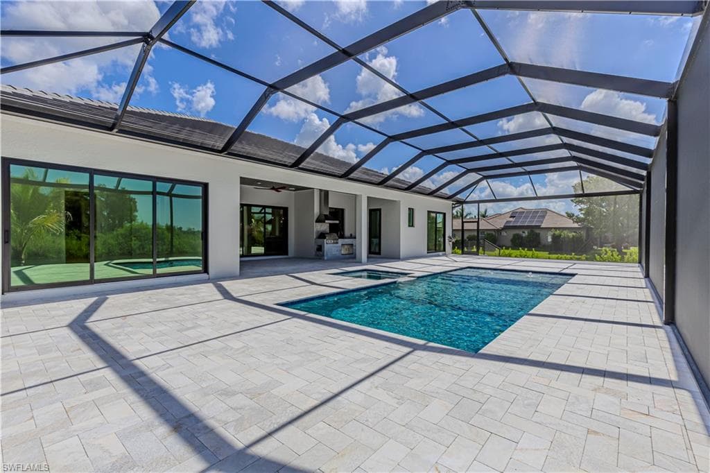 Expansive screened enclosure featuring a rectangular pool with an integrated spa, paver decking, and a built-in outdoor kitchen with a range hood