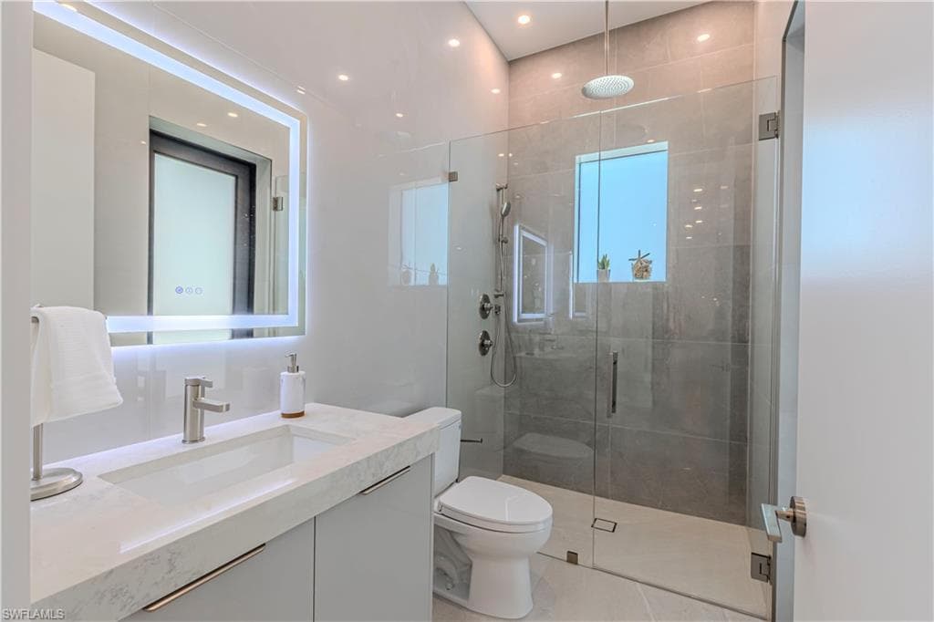 Bathroom featuring a frameless glass shower enclosure, a wall-mounted showerhead, and light gray wall tiles