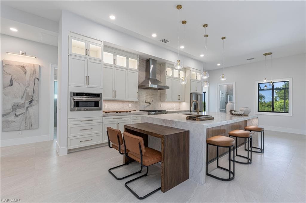 Contemporary kitchen featuring a waterfall-edge island with seating, integrated stainless steel appliances, white shaker cabinetry with glass accents, a tile backsplash, and recessed lighting