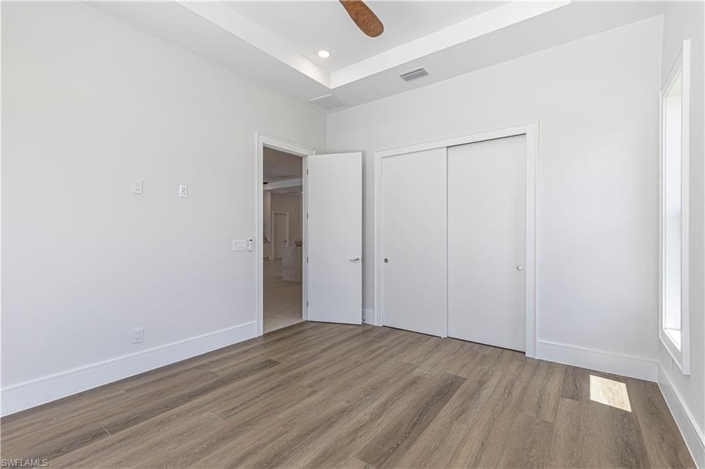 Spacious room featuring wood-finish flooring, a tray ceiling, and a ceiling fan