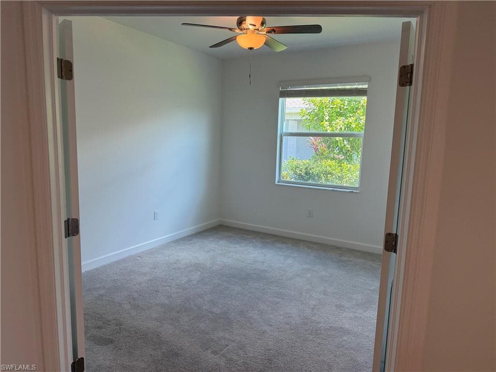 Carpeted interior room with a ceiling fan light fixture, white walls, and a window featuring blinds
