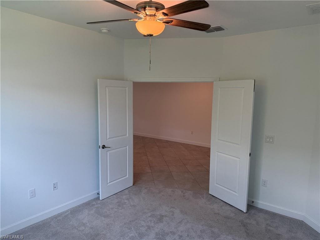 Interior space featuring a ceiling fan with light fixture, light gray carpeting, and white baseboards