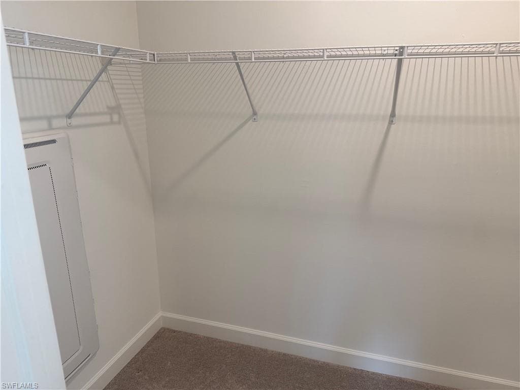 Walk-in closet featuring wire shelving, wall-to-wall carpeting, and white baseboards