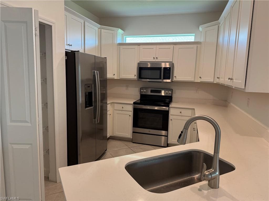 Modern kitchen featuring white cabinetry, stainless steel appliances, light-toned countertops, a stainless steel sink with a gooseneck faucet, and a pantry with shelving