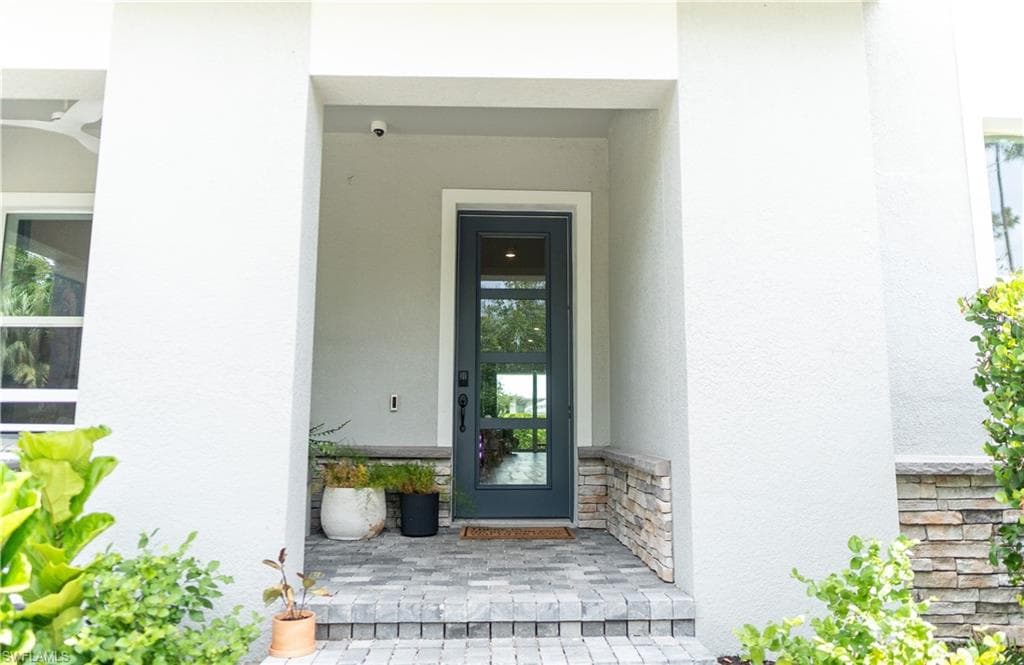 Entryway featuring a dark-framed glass panel door, stacked stone accents, textured stucco exterior, and paver steps