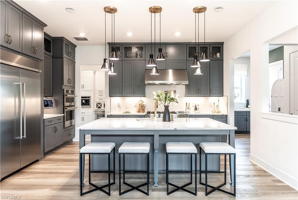 Contemporary kitchen featuring a large central island with seating, stainless steel appliances, grey cabinetry, and wood-finish flooring