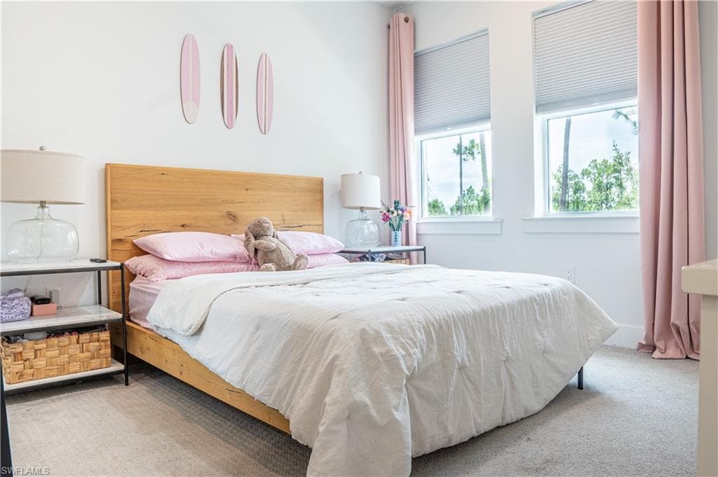 Bedroom featuring a wood-finish bed frame, light-toned carpet flooring, and white walls