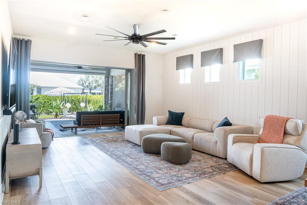 Open-concept living space featuring wood-finish flooring, white shiplap accent wall, and a multi-blade ceiling fan