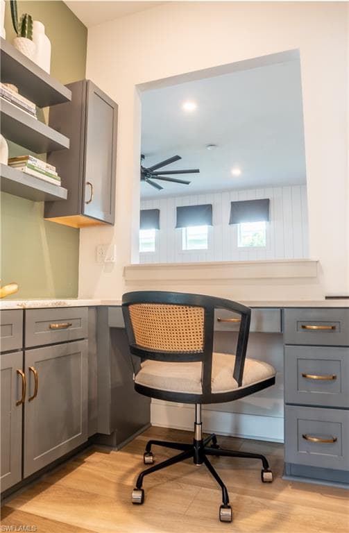Built-in desk area featuring grey cabinetry with gold-tone hardware, a light-toned countertop, and wood-finish flooring