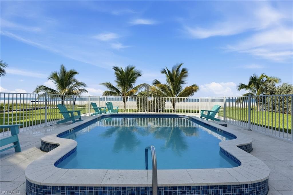 Fenced in-ground pool with integrated steps, surrounded by a paved patio and manicured lawn - Virtually Edited Image