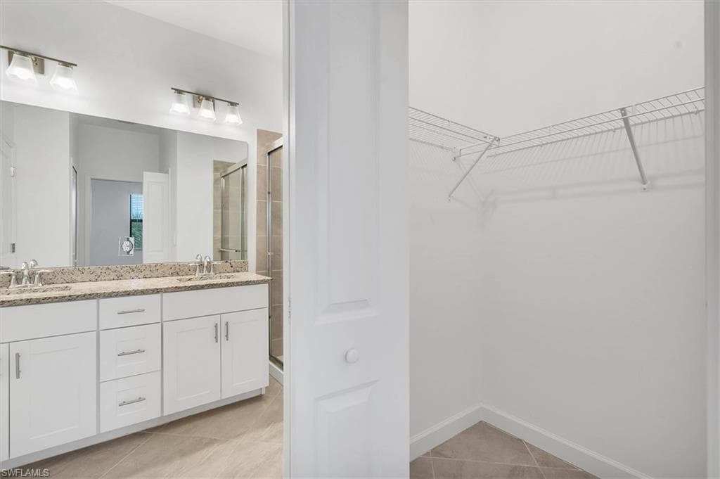 Bathroom with a stall shower, light tile patterned flooring, a walk in closet, and double vanity