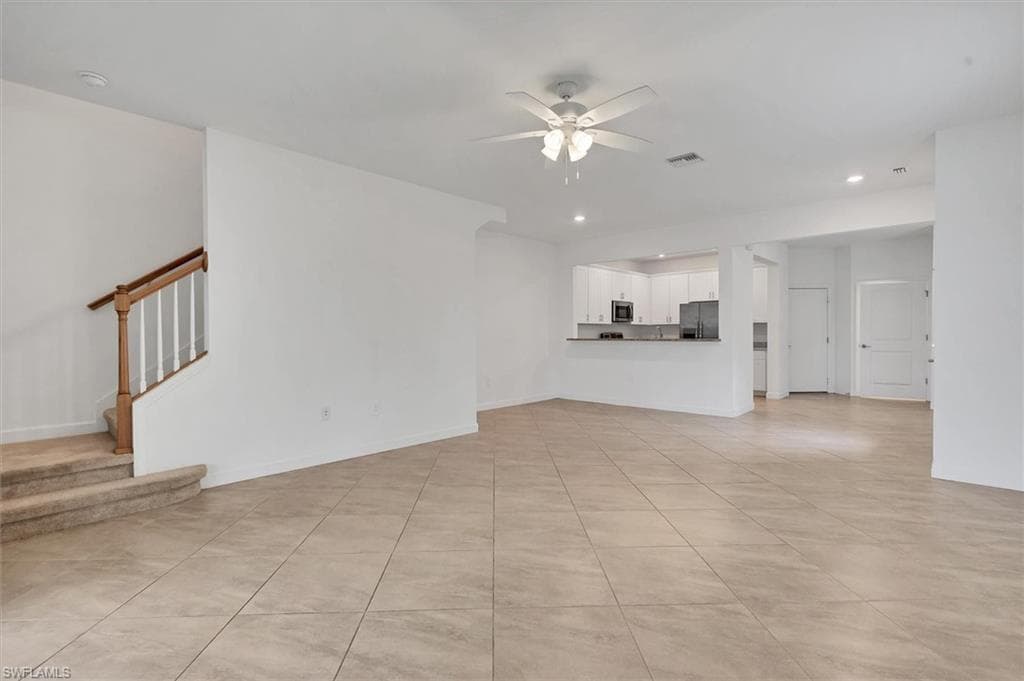 Unfurnished living room with light tile patterned flooring, recessed lighting, ceiling fan, and stairway