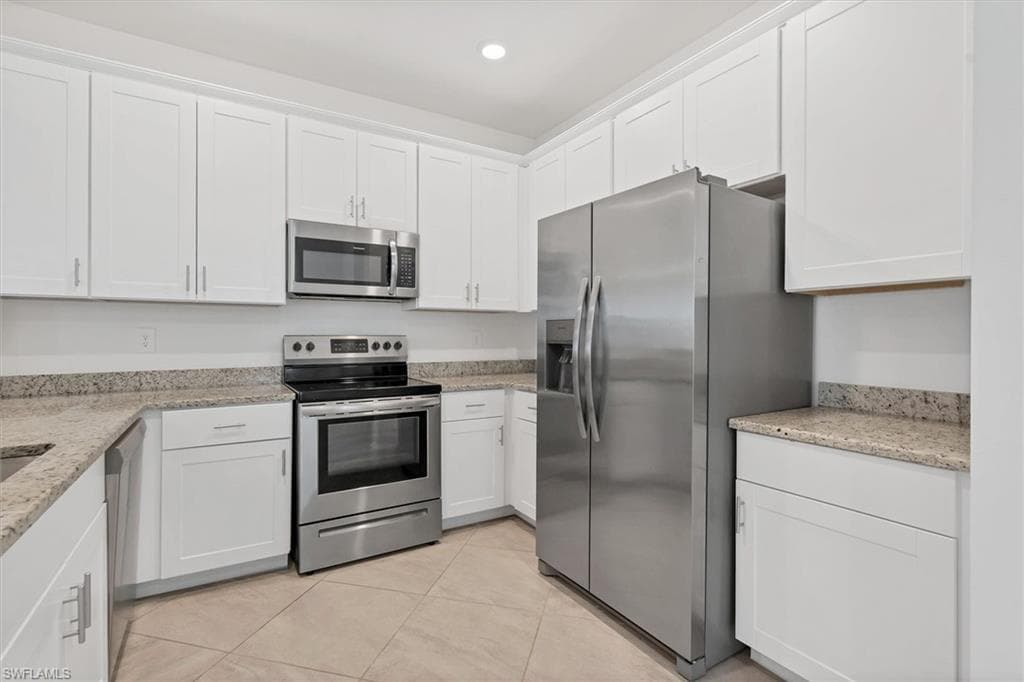 Kitchen featuring appliances with stainless steel finishes, light stone counters, white cabinetry, and recessed lighting