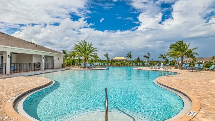 Expansive resort-style swimming poolfeaturing a curved design and a surroundingpaver deck, lined with palm trees and loungechairs