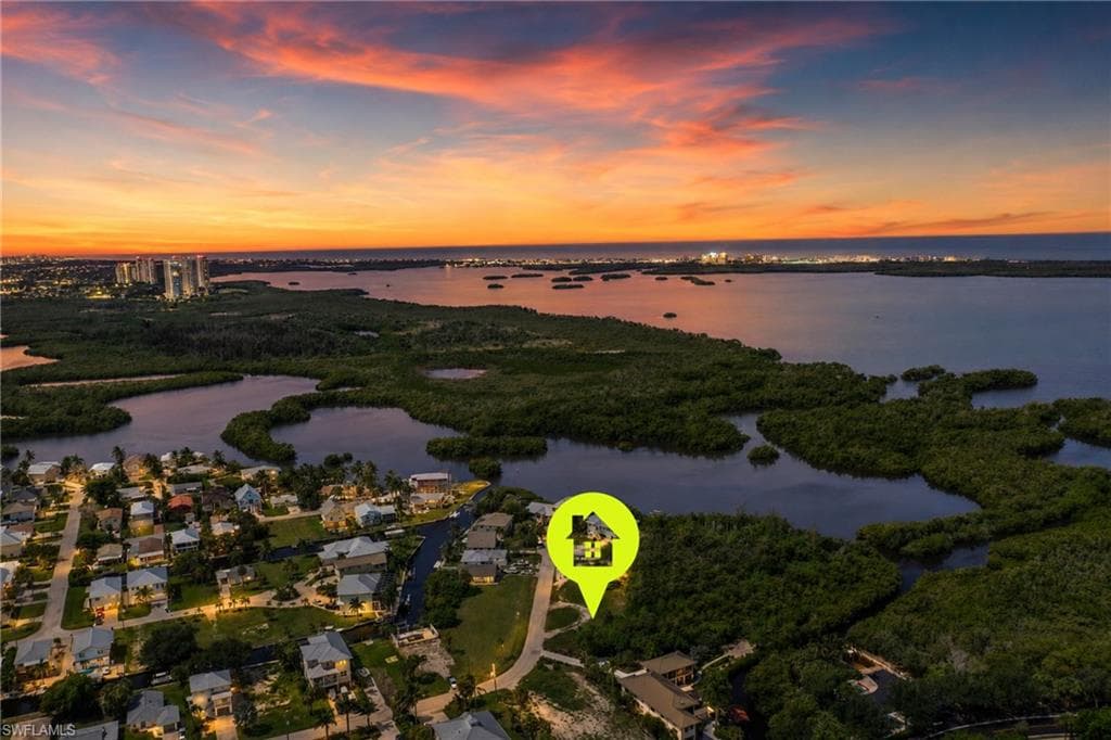 Aerial perspective with waterfrontage, featuring residential properties, lush green landscaping, and distant urban lights under a colorful sky