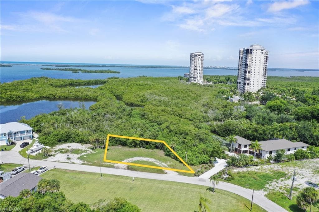 Vacant lot with partial vegetation, featuring a clear patch of land, bordered by a road, and surrounded by lush green foliage